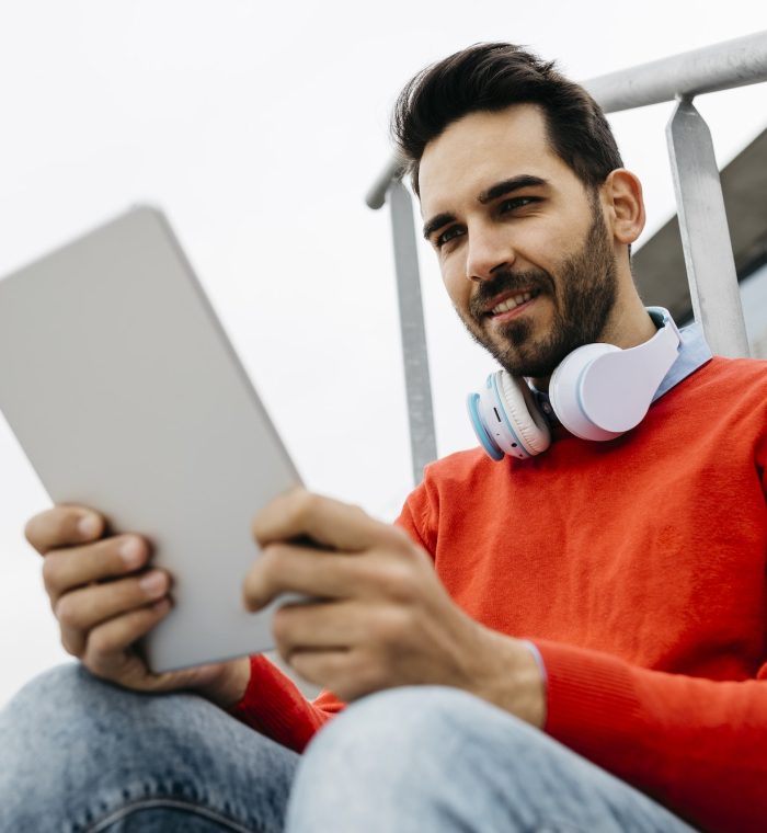 Casual businessman sitting stairs in the city, using his digital tablet and headphones